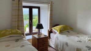 A bedroom with two beds, a nightstand, a lamp, and a window with curtains. - 2 bedroom accommodation in Crosthwaite (Crosthwaite)