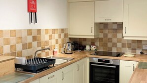 A kitchen with white cabinets, a black oven, a stainless steel sink, and a red fire blanket on the wall. - 2 bedroom accommodation in Crosthwaite (Crosthwaite)