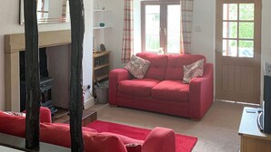 A living room with a red sofa, a fireplace, and a door with a window. - 2 bedroom accommodation in Crosthwaite (Crosthwaite)