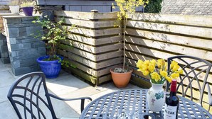 A patio with a round metal table, two chairs, a bottle of wine, and a vase with yellow flowers. - 2 bedroom accommodation in Crosthwaite (Crosthwaite)