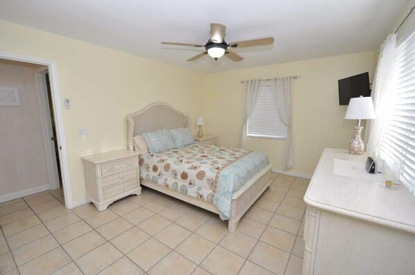 A bedroom with a bed, nightstands, a ceiling fan, a window with blinds, and a TV on the wall. - Cayman Cottage | 3 bed/2 bath canalfront home (Ramrod Key)