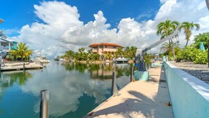 A marina with boats, a large house with a red roof, and palm trees.