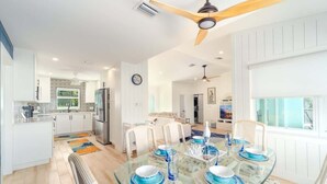 A modern kitchen with white cabinets, a stainless steel refrigerator, and a dining area with a glass table set for four.