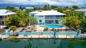 A two-story house with a swimming pool, surrounded by palm trees and other greenery.