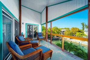 A balcony with wicker furniture, a glass door, and a view of a water body and greenery. - Foster's Folly | Gorgeous canalfront pool home (Summerland Key)