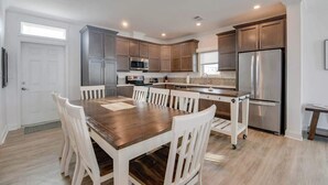 Una cocina moderna con armarios de madera, un refrigerador de acero inoxidable y una zona de comedor con mesa de madera y sillas blancas.
