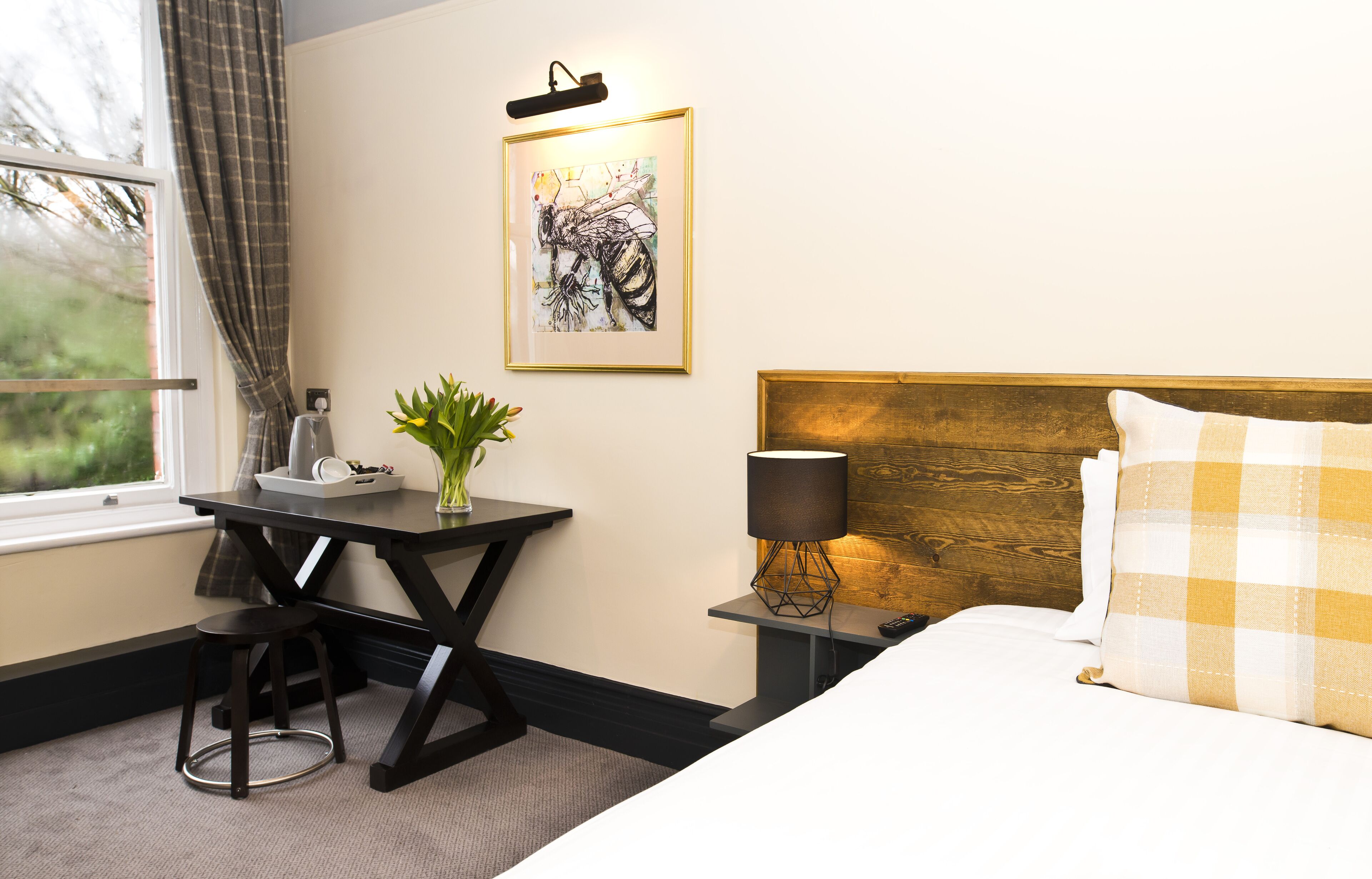 Une chambre d’hôtel avec un lit, un bureau doté d’une lampe, une œuvre d’art encadrée au mur et une fenêtre avec des rideaux.
