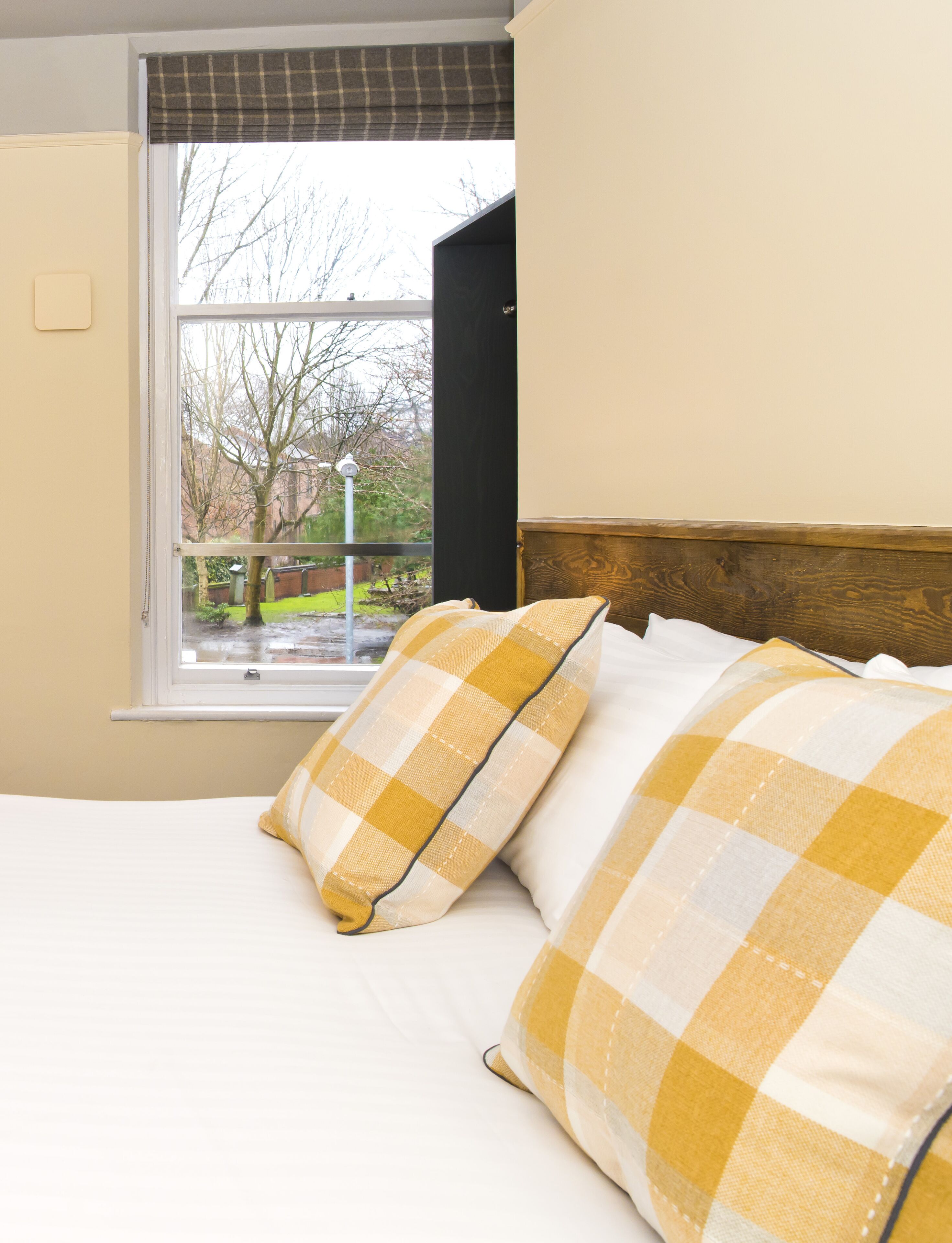 A bedroom with a bed, two pillows, a window, and a view of a garden.