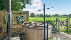 Een houten jacuzzi met metalen steunpoten, een metalen barbecue en een houten terras.