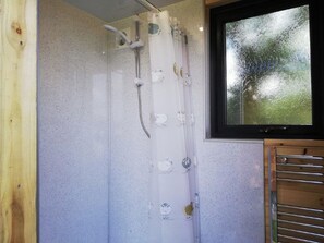 Une douche avec un rideau, une fenêtre donnant sur les arbres et une porte en bois.