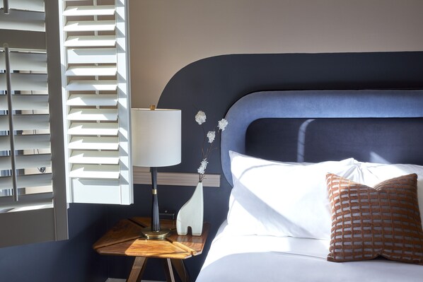 A neatly made bed with white and brown pillows, a bedside table with a lamp, and a vase with flowers. - The Oliver Hotel (Knoxville)