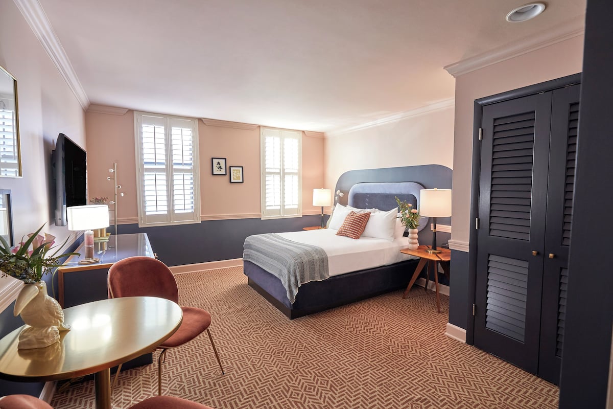 Habitación de hotel con una cama grande, un escritorio con lámpara, una silla y un televisor.
