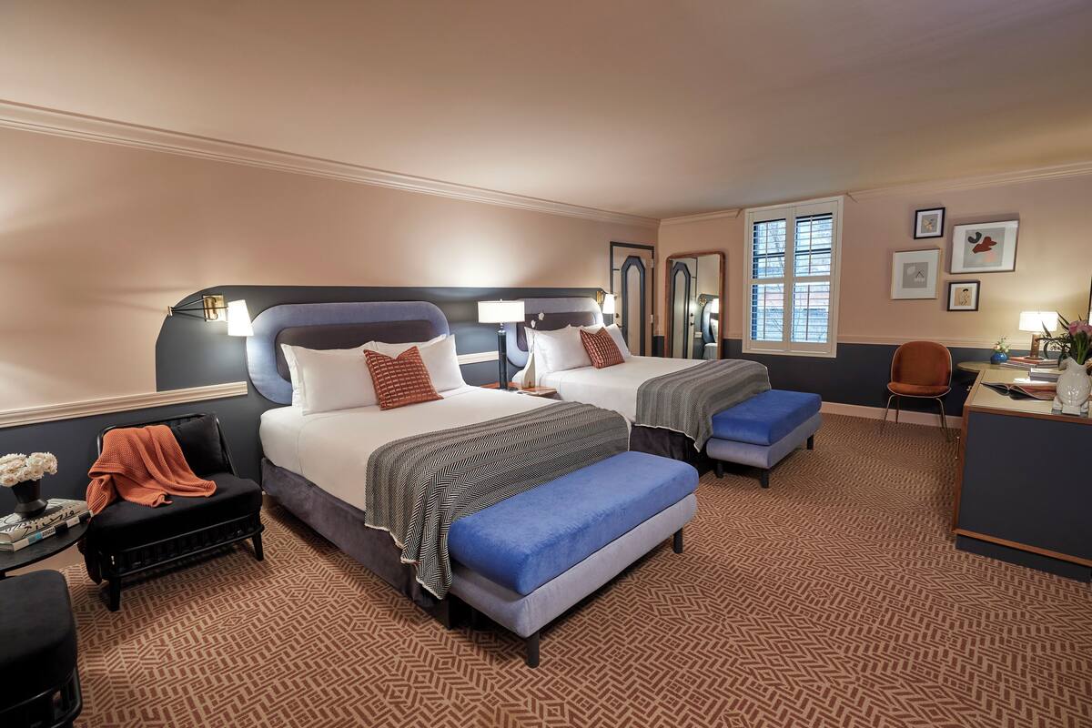 Habitación de hotel con dos camas, un escritorio, una silla y un pequeño rincón de descanso.