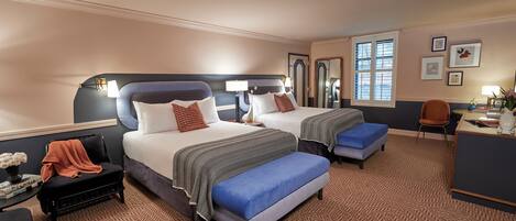 A hotel room with two beds, a desk, a chair, and a small seating area.