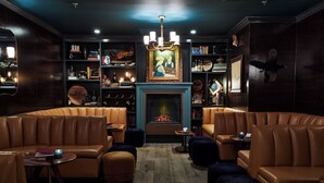 Un espace salon confortable avec des fauteuils en cuir, une cheminée et une bibliothèque remplie de livres et d’objets décoratifs.