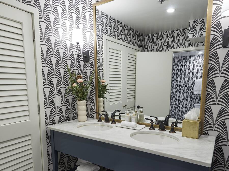 Un baño con lavamanos doble, un espejo grande y papel tapiz estampado.