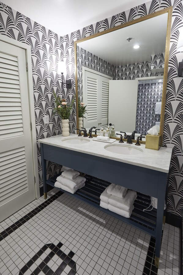 A bathroom with a double sink, a large mirror, and patterned wallpaper. - The Oliver Hotel (Knoxville)