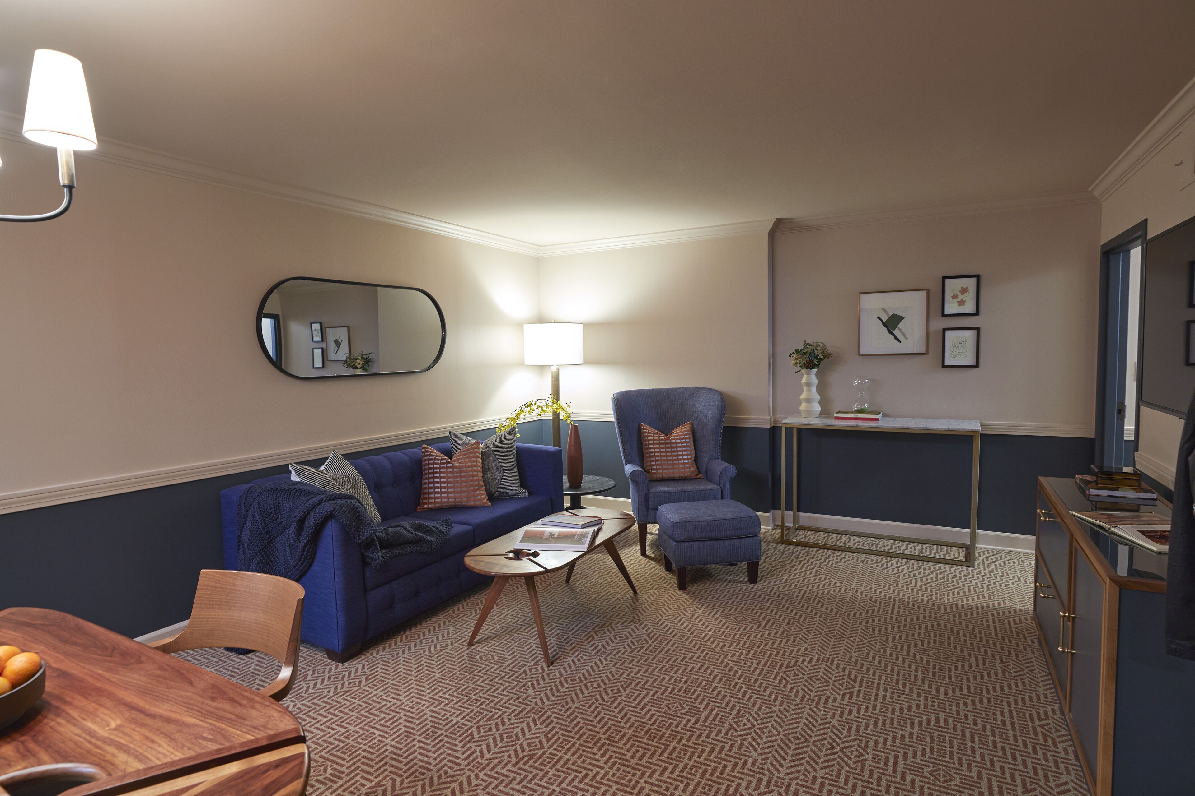 A living room with a blue sofa, armchairs, a coffee table, and a dining table with oranges.