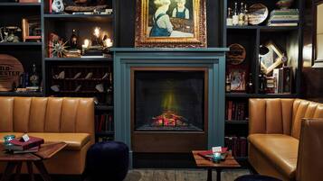 Una biblioteca acogedora con sofás de cuero, chimenea y estanterías llenas de libros y objetos decorativos.