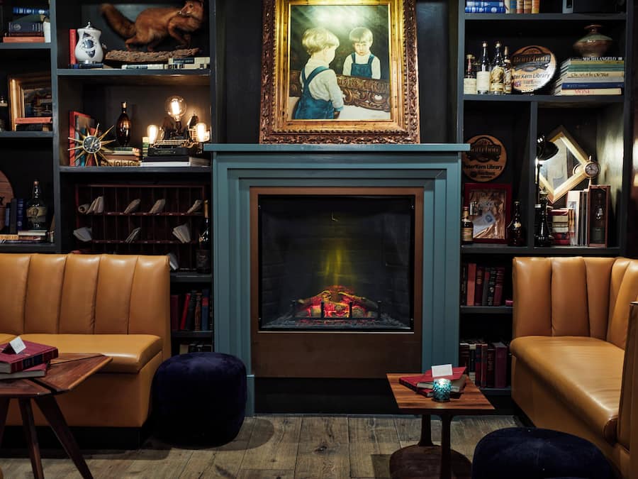 Una biblioteca acogedora con sofás de cuero, chimenea y estanterías llenas de libros y objetos decorativos.