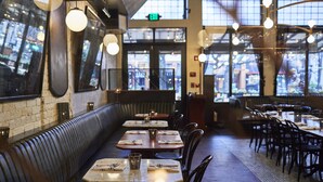 L’intérieur d’un restaurant avec des banquettes et des tables, un mur en briques et de grandes fenêtres.
