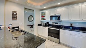 Una cocina moderna con armarios blancos, encimera de granito negro, electrodomésticos de acero inoxidable y un espejo decorativo.