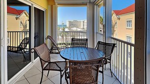 A balcony with a round table and wicker chairs, overlooking a residential area with buildings and a clear sky. - Bella Lago 241 by Distinctive Beach Rentals (Fort Myers Beach)
