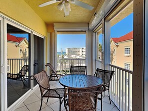 A balcony with a round table and wicker chairs, overlooking a residential area with buildings and a clear sky. - Bella Lago 241 by Distinctive Beach Rentals (Fort Myers Beach)