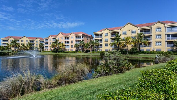 A hotel with multiple buildings, a pond with a fountain, and palm trees. - Bella Lago 241 by Distinctive Beach Rentals (Fort Myers Beach)