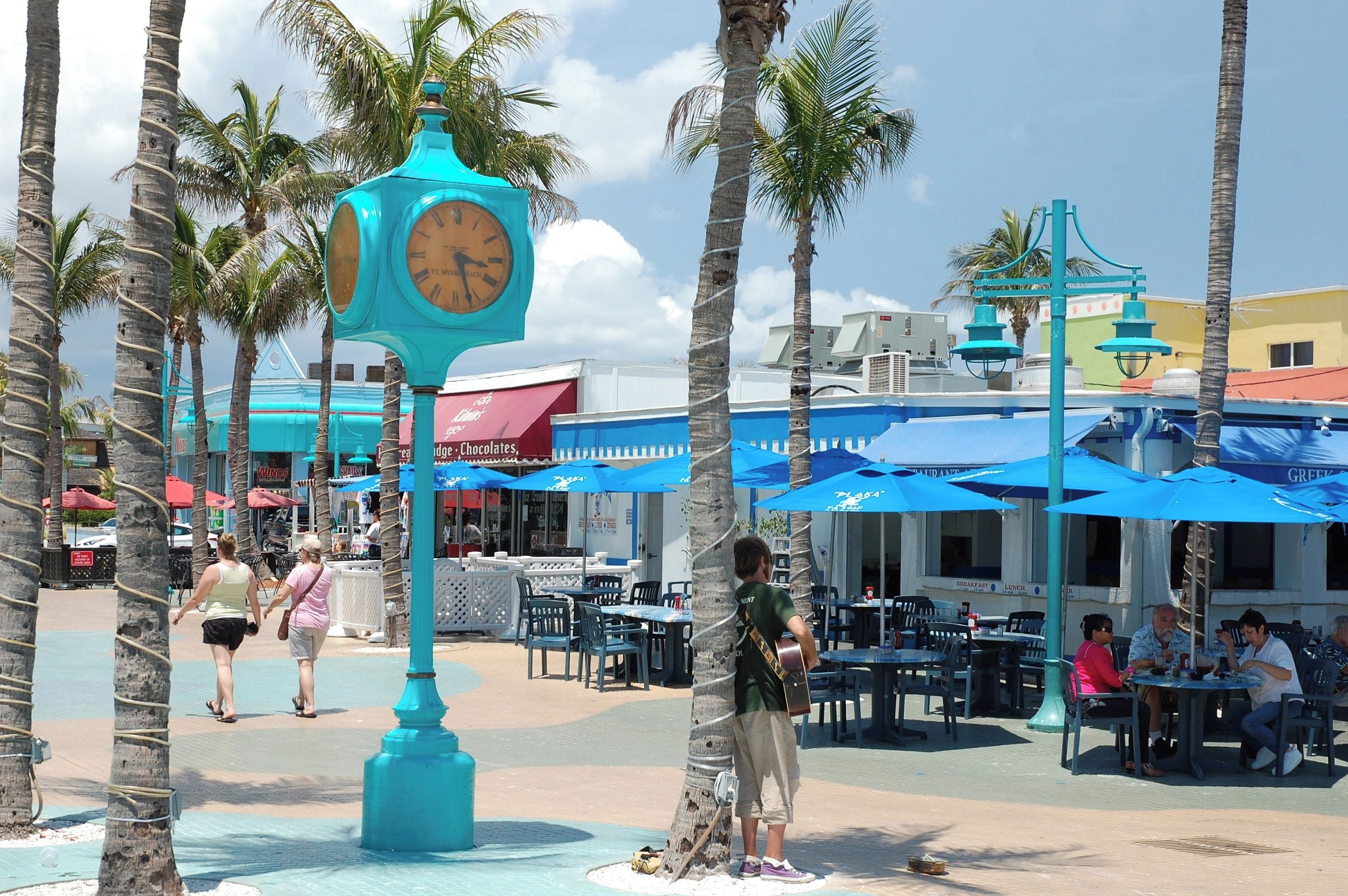 A public square with palm trees, outdoor seating, and a clock.