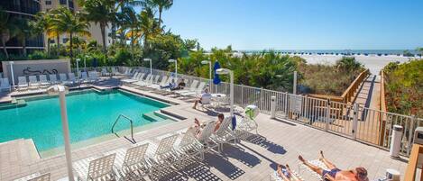 A pool area with lounge chairs and a view of the beach.