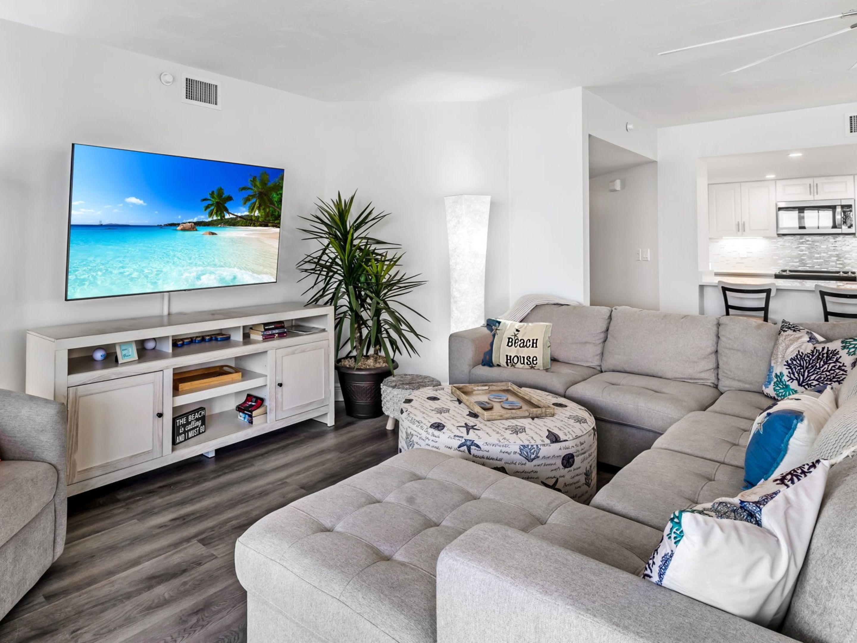 A modern living room with a flat-screen TV, a grey sofa, a coffee table, and a potted plant.