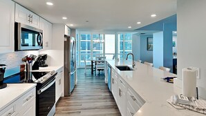 A modern kitchen with white cabinetry, stainless steel appliances, and a large island with a sink. - Gullwing 405 by Distinctive Beach Rentals (Fort Myers Beach)
