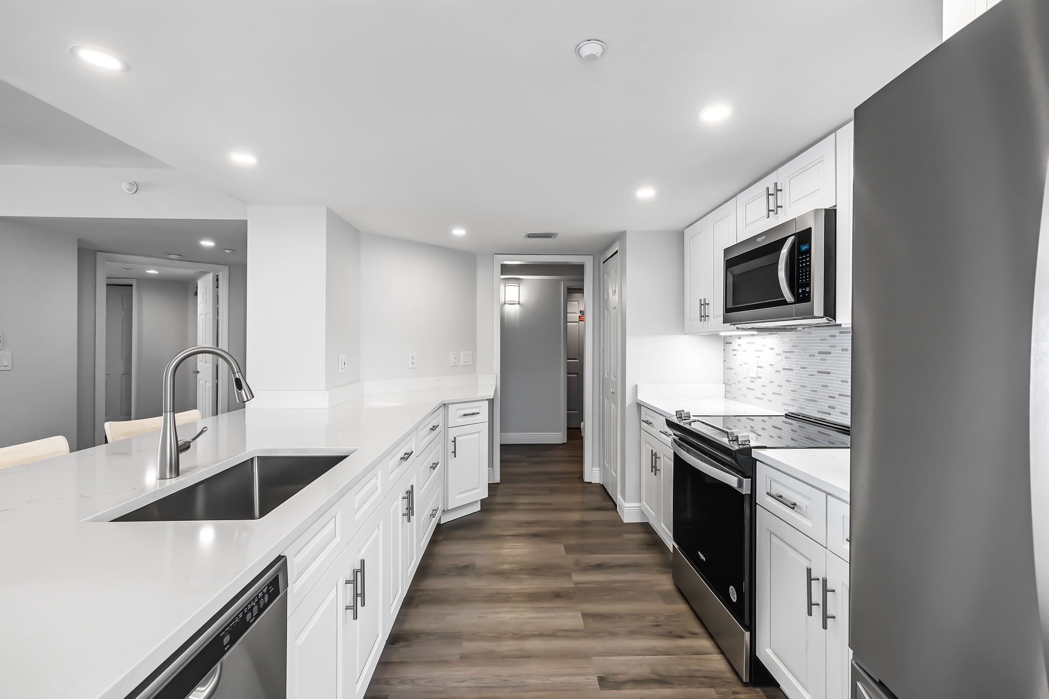 A modern kitchen with white cabinetry, a stainless steel sink, a built-in microwave, and a dishwasher.