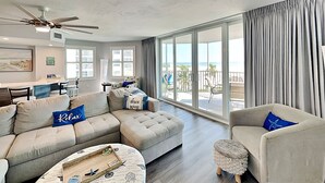 A spacious living room with a large sectional sofa, a round coffee table, and a view of the ocean through large windows. - Gullwing 405 by Distinctive Beach Rentals (Fort Myers Beach)