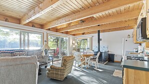 A cozy cabin interior with a dining area, kitchen, and large windows offering a view of the outdoors.