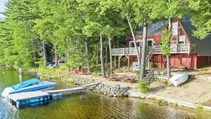 A lakeside cabin with a dock, a boat, and a deck area with chairs and a small boat.