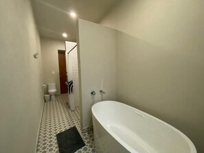Ein schmales Badezimmer mit einer weißen Badewanne, einer Toilette und einer Duschkabine.