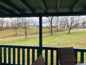 A covered outdoor seating area with a view of a grassy field and trees.