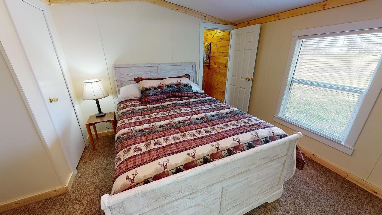 Un dormitorio con una cama, una mesita de noche, una lámpara, una ventana y una puerta.