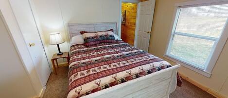 A bedroom with a bed, a nightstand, a lamp, a window, and a door.
