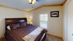 Un dormitorio con cama, ventana, un cuadro en la pared y ventilador de techo.