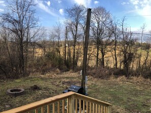 A wooden deck with a grill and a fire pit in a rural outdoor setting.