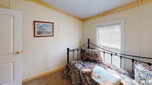 A bedroom with a bed, a door, a window with blinds, and a framed picture on the wall.