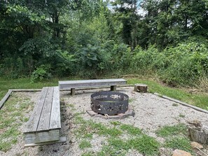 A picnic area with a wooden bench and a fire pit.