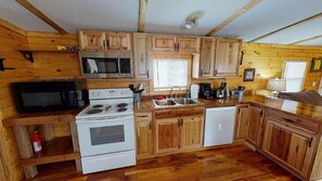 A compact kitchen with wooden cabinets, a microwave, a stove, a sink, and a dishwasher.