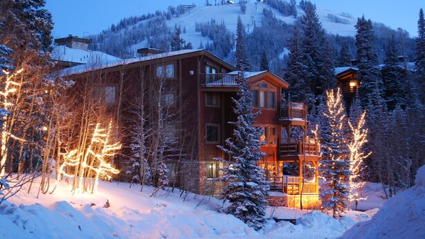 En snedækket hytte med træfacade, en balkon og en skilift i baggrunden.