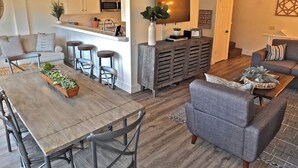 Ein modernes Wohnzimmer mit einem grauen Sofa, einem Holzesstisch mit Stühlen und einer Küche im Hintergrund.