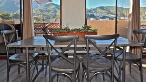 Ein Essbereich mit Tisch und Stühlen, einer Kandelaberleuchte und Blick auf eine Berglandschaft durch große Fenster.