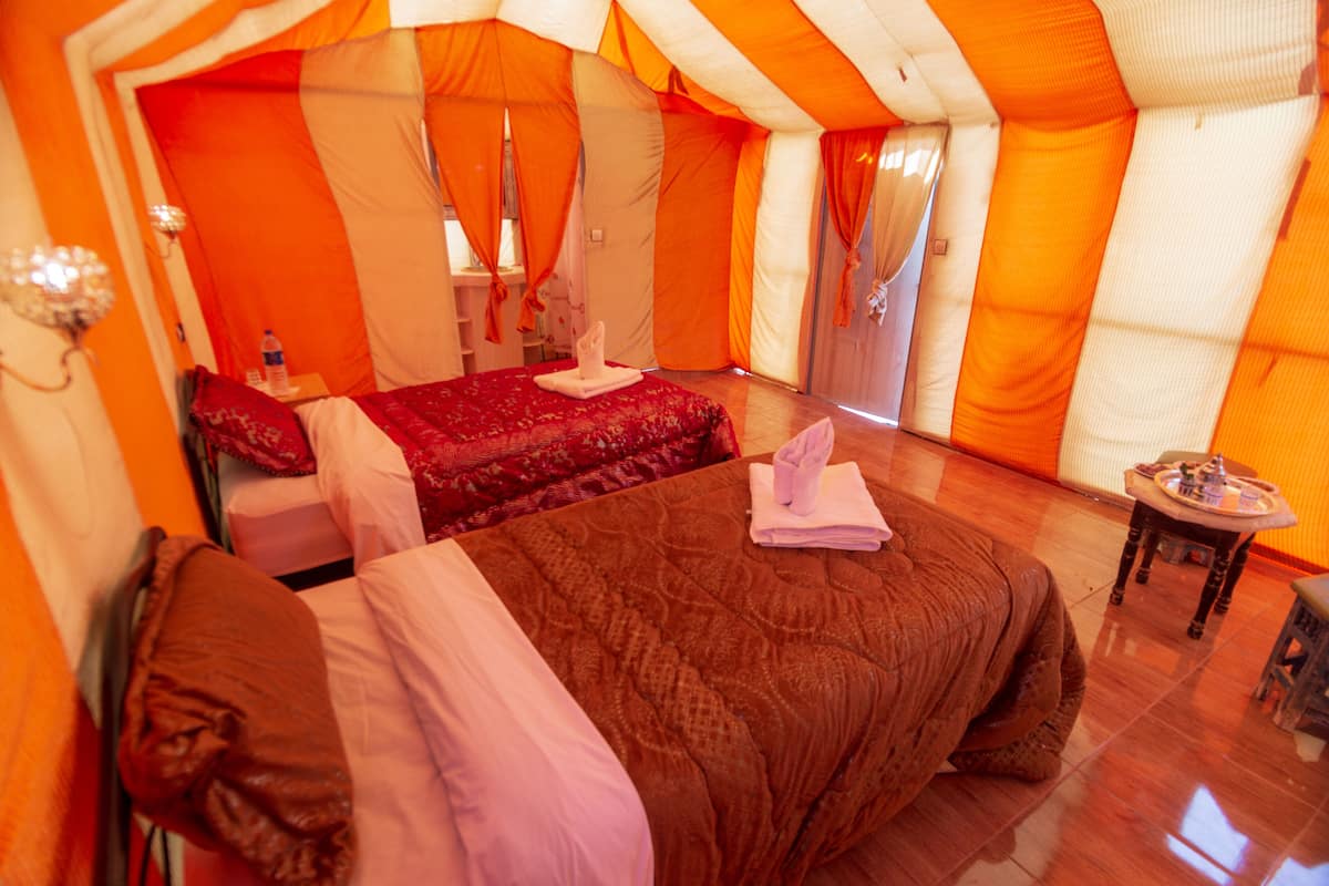 A tent-style room with two beds, a small table, and a mirror.